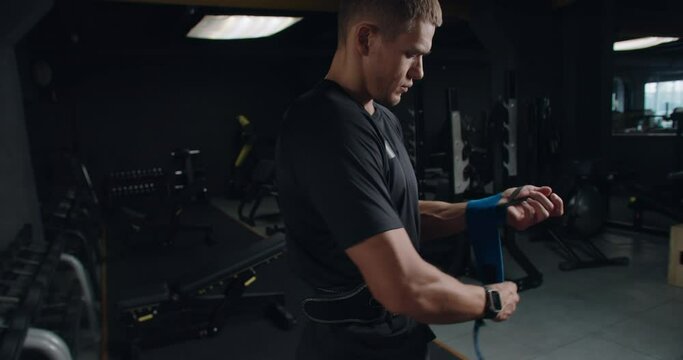 Athletic man put wrist straps on hands, preparing for power training with weight lifting. Young male sportsman has workout at gym. 