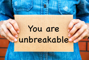 Woman holding a piece of a cardboard with words You Are Unbreakable