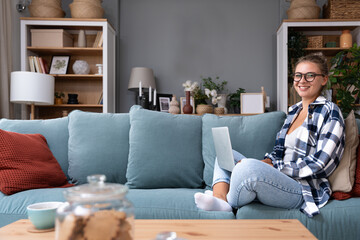 Young woman lying on couch in living room work online on laptop gadget. Millennial female relax rest on sofa at home look at computer screen text message on device. Business communication concept.