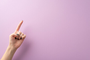 From first person top view, the hand of a young lady, complete with stylish black manicure, creates a pointed gesture using her index finger. The lilac background provides text or ad placement
