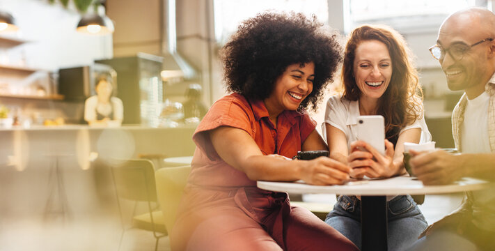 Happy friends using a smartphone together over lunch in a coffee shop