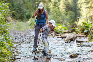 Young woman fording the stream with her son in mountains