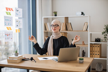 Businesswoman meditating in office chair behind computer