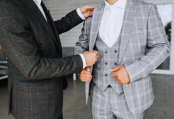 A friend of the groom helps the groom in a stylish gray suit in preparation for the wedding in the...