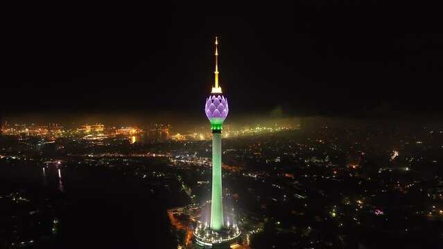 Night aerial footage of famous Lotus Tower illuminated by changing colour neon lights. Logistic terminal in seaport glowing into dark. Colombo, Sri Lanka