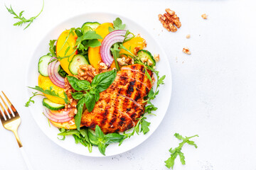 Delicious healthy salad with peaches, grilled chicken breast, cucumber, walnuts, red onion, green basil and mixed herbs, white table background, top view