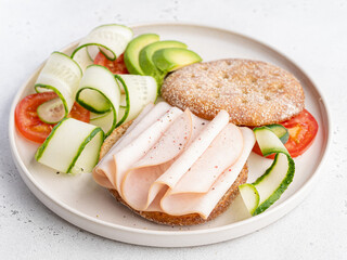 Open sandwich with turkey or chicken ham, sliced cucumber, avocado pieces and fresh tomatoes on white ceramic plate. Top view table. Healthy eating concept. Copy space. Vegetable and oat bread lunch.