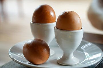 Boiled eggs in a white cup on a wooden table in the kitchen,Fresh soft boiled egg in cup on grey...