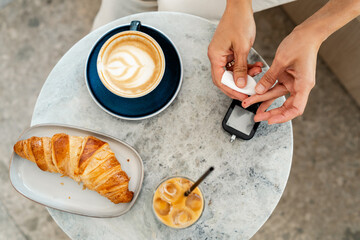 Woman checking blood sugar level.  Expected Blood Glucose After a High-Carb Meal.  milk coffee and ice cubes, and freshly baked croissants on marble plate