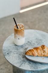 Still life shot of iced coffee and croissant at marble table