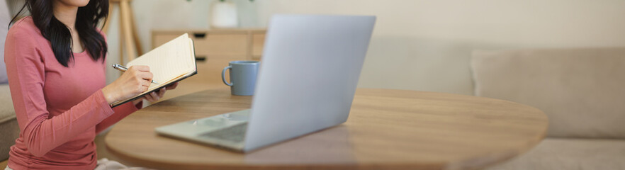 Young businesswoman working at home to reading business data on laptop and writing note in notebook