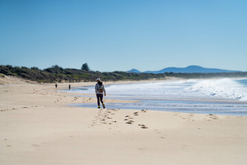 Naklejka premium couple walking on the beach, women in coats and beanies walk down a winter beach in hobart tasmania, australia.