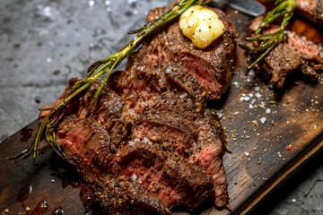 Grilled medium rare sliced meat steak, on a wooden serving board, with rosemary red tomatoes, on a black wooden table backgroun