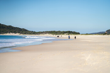 walking on Sandy beach, next to the sea with waves breaking behind, and mountains in the distance