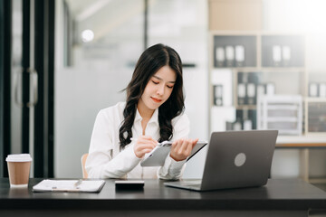 Successful Asian Businesswoman Analyzing Finance on Tablet and Laptop at Office Desk tax, report, accounting, statistics, and analytical research concept.