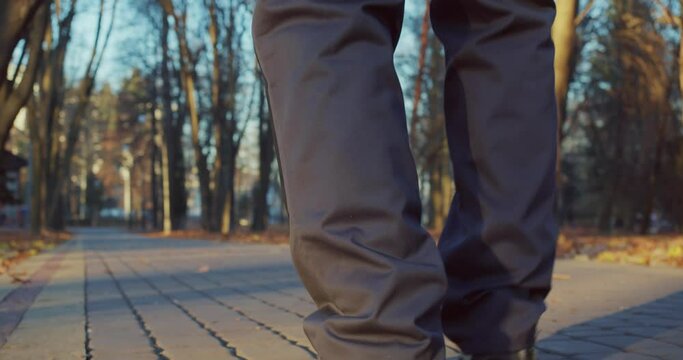 Close up of janitor in uniform and shoes walking among autumn city park. Focus on male legs. Outdoors work. 