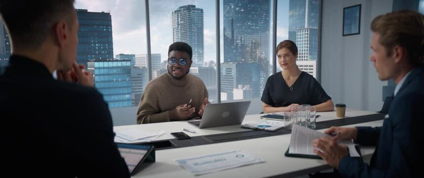 Office Conference Room Meeting: Diverse Team of Top Managers Talk, Brainstorm, Use Tablet and Laptop. Black Entrepreneur Presenting Investment Strategy to Investors, Discussing Ideas. Anamorphic Shot