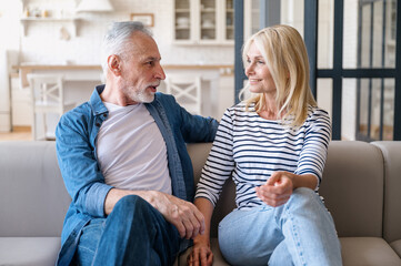 Mid age couple enjoy conversation sitting on sofa in living room