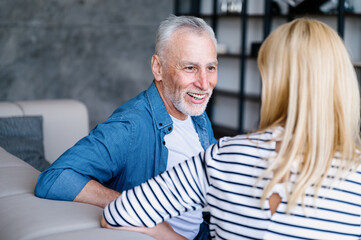 Senior man telling joke to woman in living room at home.