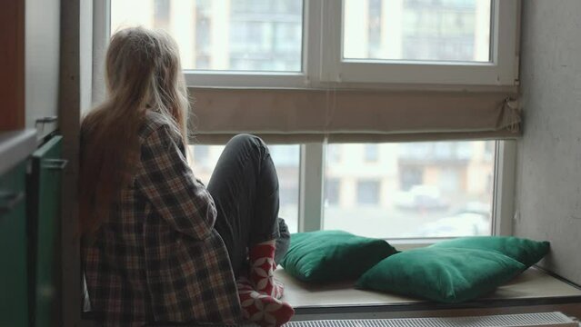 Teen girl sits on the windowsill and reads a book