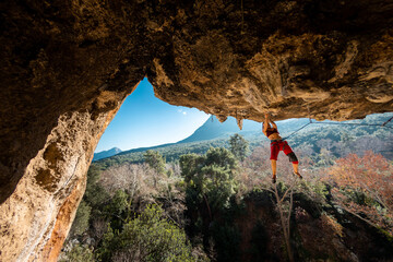 Girl climber on an overhanging rock. A sports woman climbs a rock against the backdrop of...