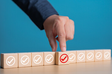 Checklist, Task list, Survey, Double check, Assessment, and Quality Control. Goals achievement and business success. Close-up hand choosing red check mark icon on wooden blocks.