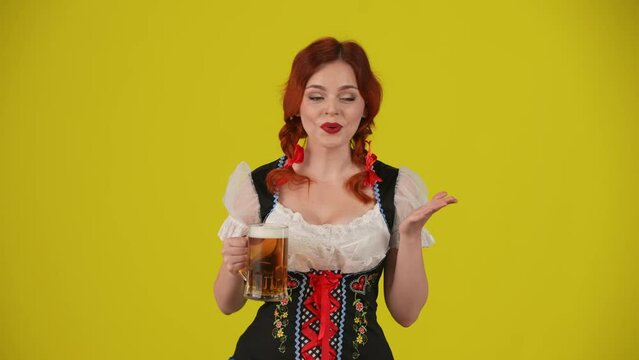 Medium yellow background isolated video of a young German woman, waitress, wearing a traditional costume, holding a glass of beer, pointing to the side of the frame, wow and excitement.