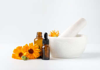 Calendula officinalis flowers in mortar and amber glass dropping bottles with essential oil on...