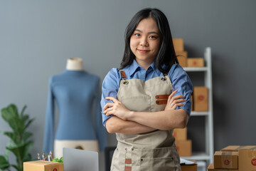 An Asian SME entrepreneur stands with his arms crossed and smiles for the camera and prepares to deliver goods to a customer at his home office. Digital technology concept SME e-commerce online.