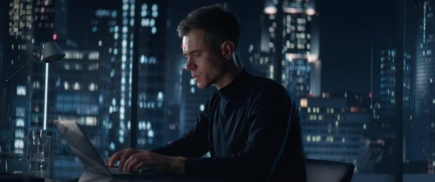 Successful Businessman Working on Laptop Computer in Big City Office Late At Night. Financial Investment Analyst Checking Data And Feeling Stressed Due To Negative Corporate Report. Anamorphic Shot