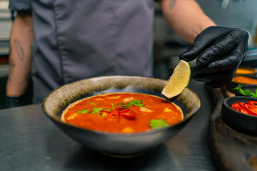 close up of delicious freshly prepared spicy red tom yum soup with seafood and lime in asian...