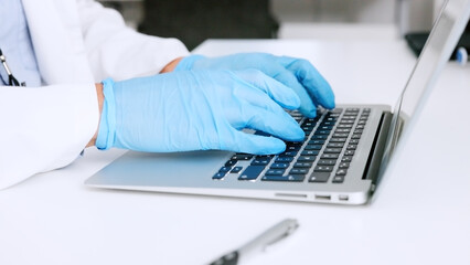 Hands of a scientist in surgical gloves, typing on a laptop in a medical lab. Closeup of a...