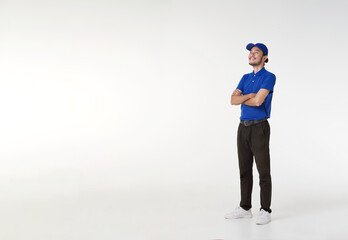 Smiling asian delivery man in blue uniform standing with arms crossed isolated on white background. looking up copy space. Full length portrait.