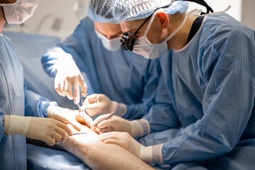 Three confident surgeons performing surgical operation on a patient's knee in operating room. Concept of real surgery and invasive treatments - 643660887