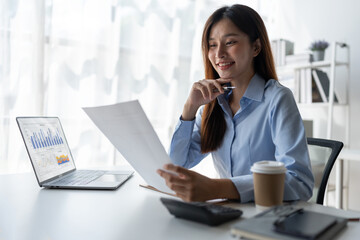Asian businesswoman holding information sheet paper Business growth graphs, charts to analyze financial reports. using laptop computers and calculators to Office investment plan