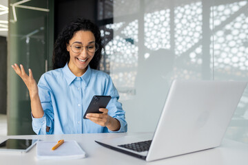 Happy and successful business woman received online notification with good news on her phone, Hispanic woman celebrating good results and online achievement, using app on smartphone inside office.