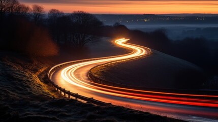 A curvy, winding country road with a path of light from leading headlights passes.