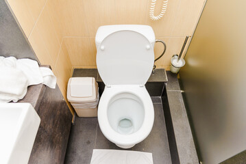 White toilet with opened lid in toilet with gray tiled wall. View of clean toilet bowl on top with...