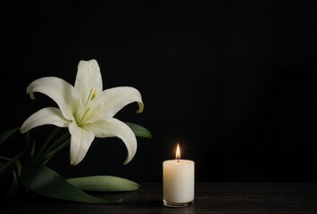 a close-up of a candle and a lily on a dark wooden table with black backdrop