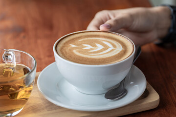 Close-up of woman's hand with cup of latte art coffee in coffee shop.