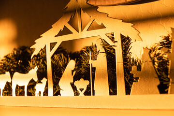 A close up of a home nativity scene surrounded by garland and bathed in later evening sun.