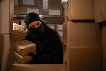A thief stealing boxes in a warehouse at night in the dark. Warehouse and store security concept