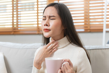 Sore throat in flu season. Young asian woman touching her neck and feeling pain in throat in the...