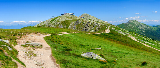 Mountain landscape on a hiking trail in the Low Tatras, Slovakia. View of mountain peaks and valleys while hiking along a mountain ridge. Slopes covered with alpine vegetation, summer sunny day.