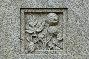 Stone carving of flowers on grave stone in cemetery.