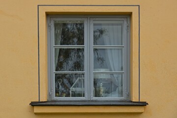 Window with grey painted frame on a yellow plastered wall and curtains inside and lamp.