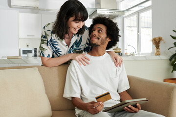 Young affectionate couple looking at one another while woman bending over her husband with tablet...