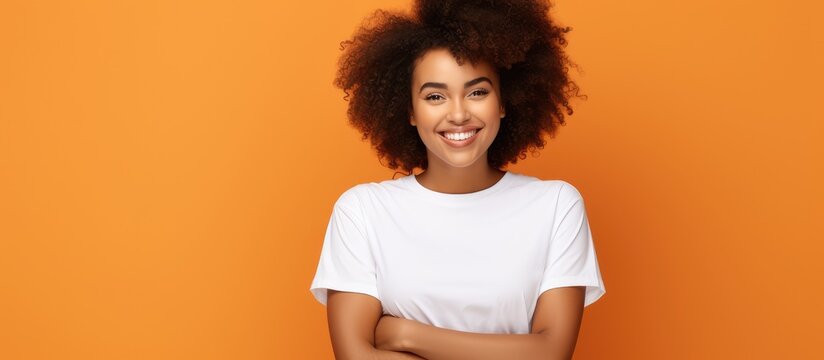 A happy black woman in a white shirt with curly hair crosses her fingers looks at empty space and stands alone on an orange background The photo promotes hope a positive lifestyle advertisement