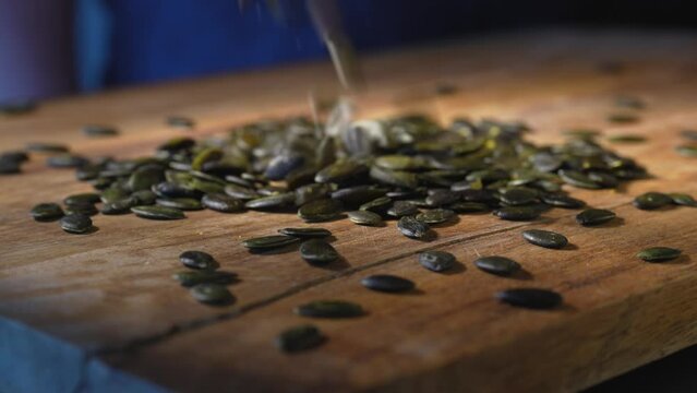 Pumpkin seeds drop from above on wooden kitchen board. Close-up.