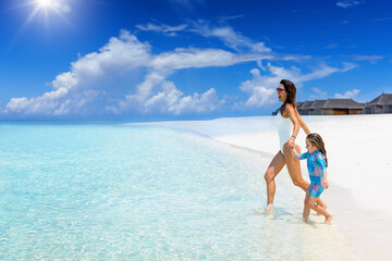 Fototapeta na wymiar A happy mother and daughter run into the turquoise sea of a tropical paradise beach